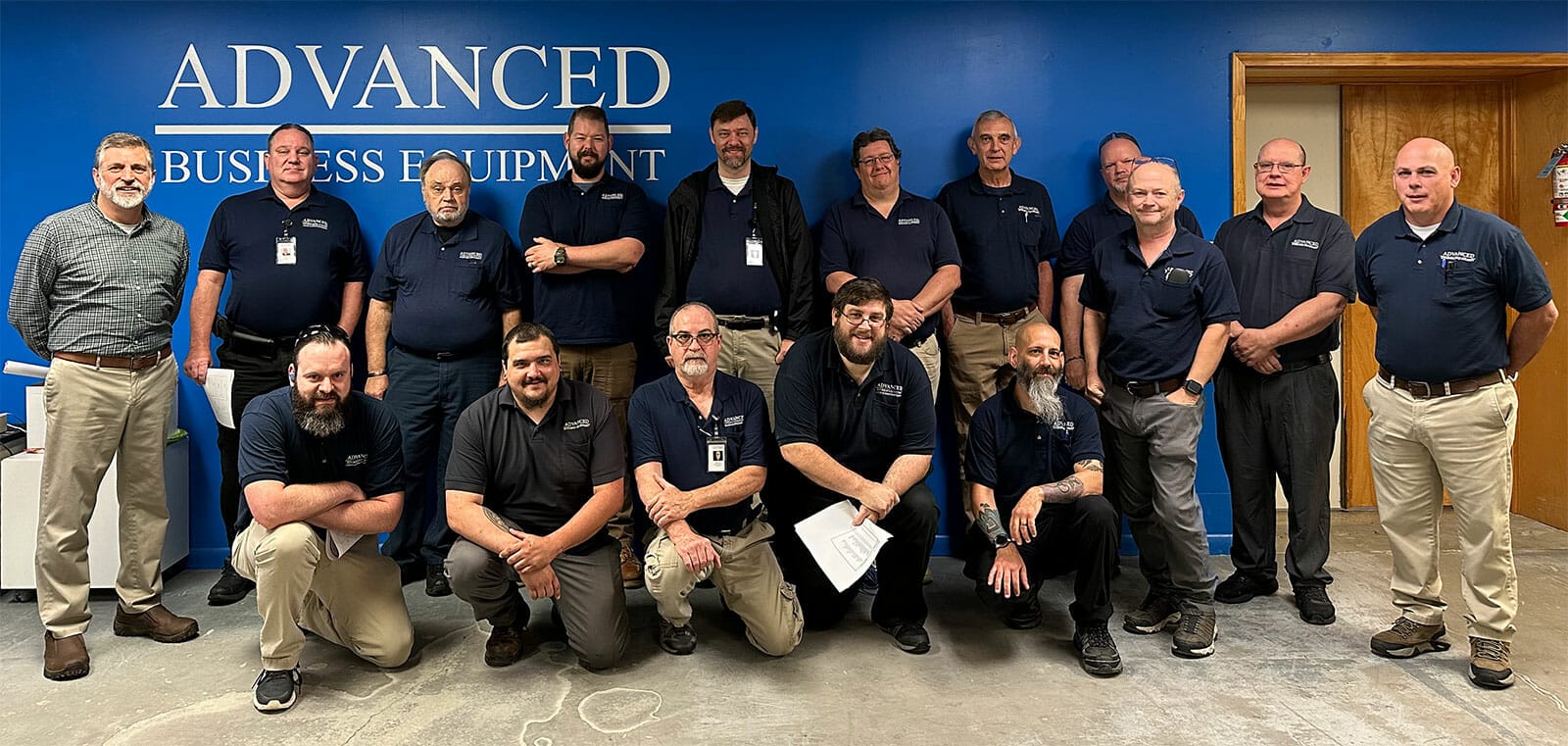 a group photo of employees standing in front of a blue wall with a white company logo