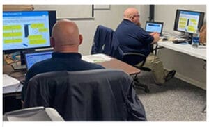 2 men seen from the back sitting and looking at computer monitors