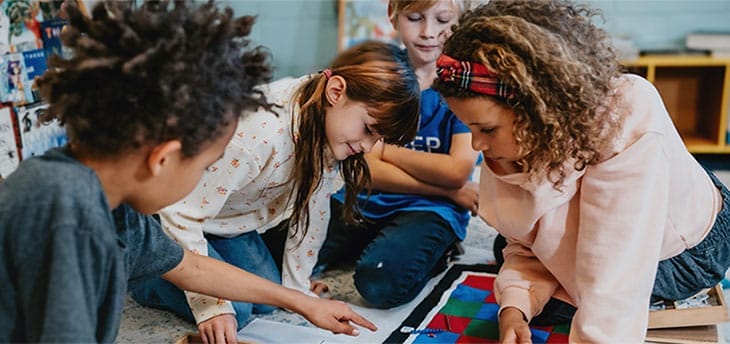 4 elementary school children play a learning game while seated on the floor