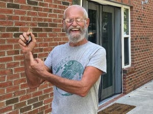 smiling man standing in front of a building door, holding up a house key